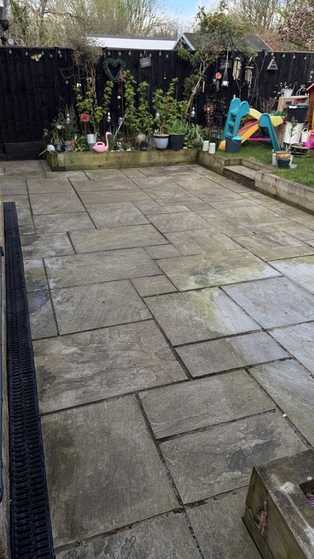 Grey patio with a children's playhouse in the garden behind, before cleaning and repointing