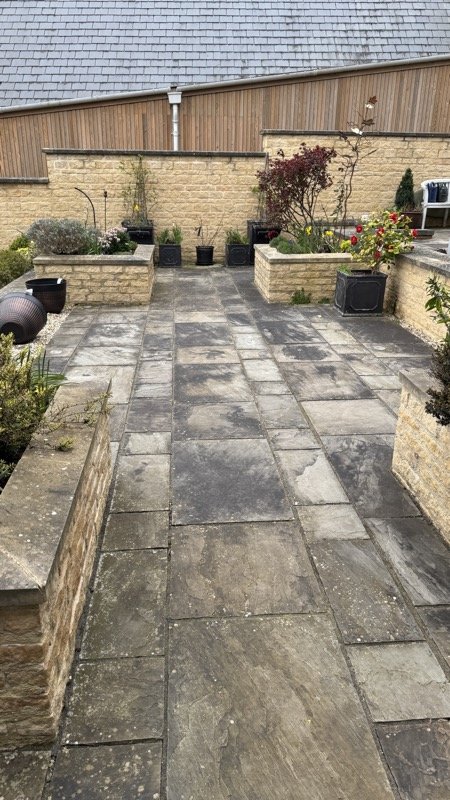 Dark, weathered patio slabs between raised stone planters before cleaning
