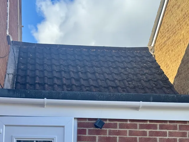 Extension roof with dark, moss-stained tiles before cleaning