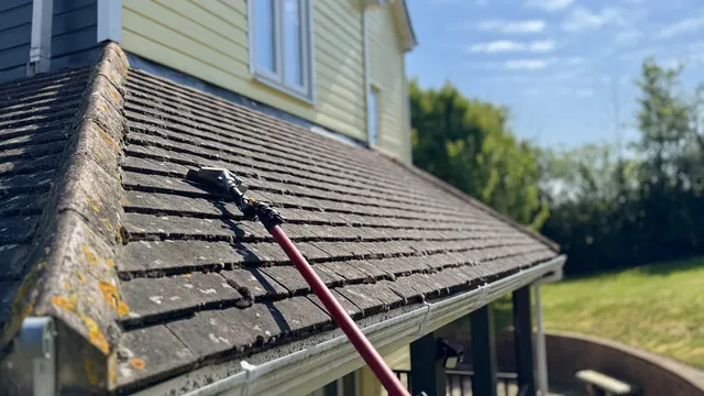 Long-reach pole being used to clean moss from a tiled roof edge