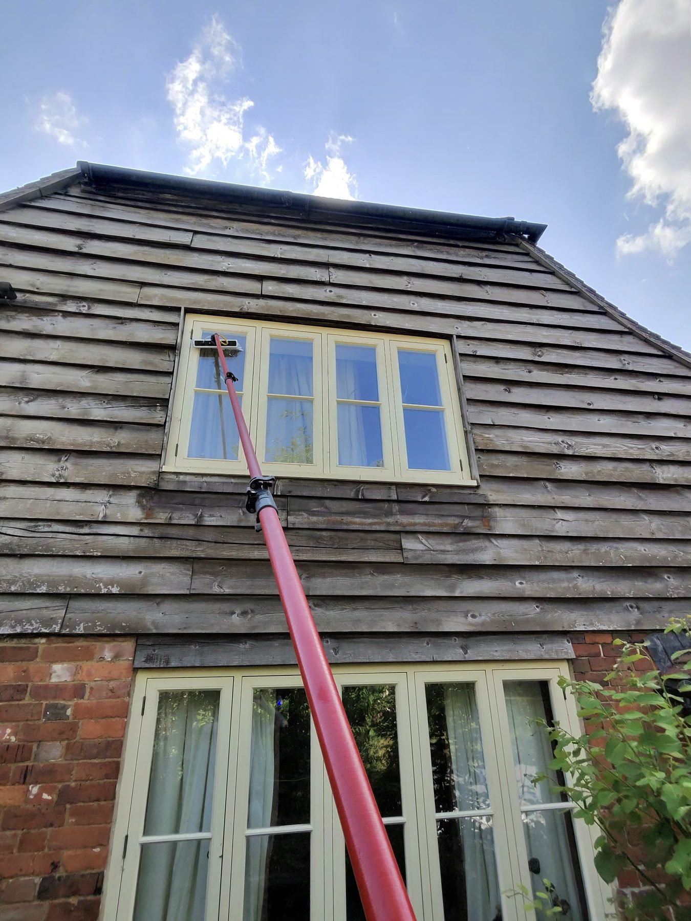 Cleaning an upstairs window on a timber-clad house with a pole